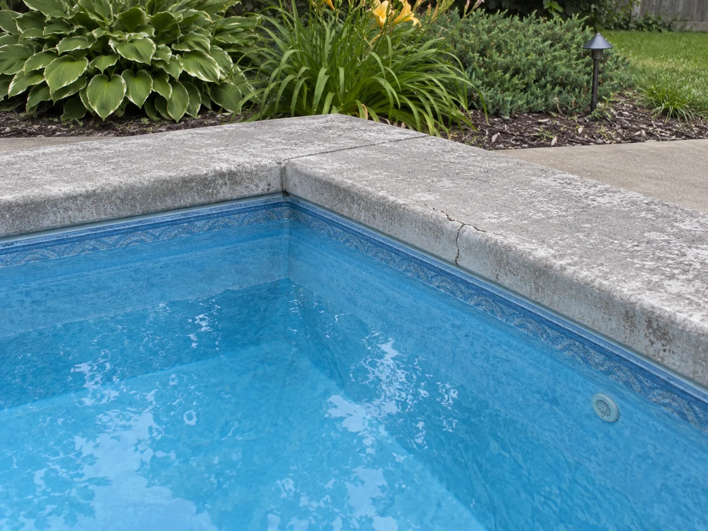 Angolo di una piscina datata con bordo segnato dal tempo e una crepa superficiale.